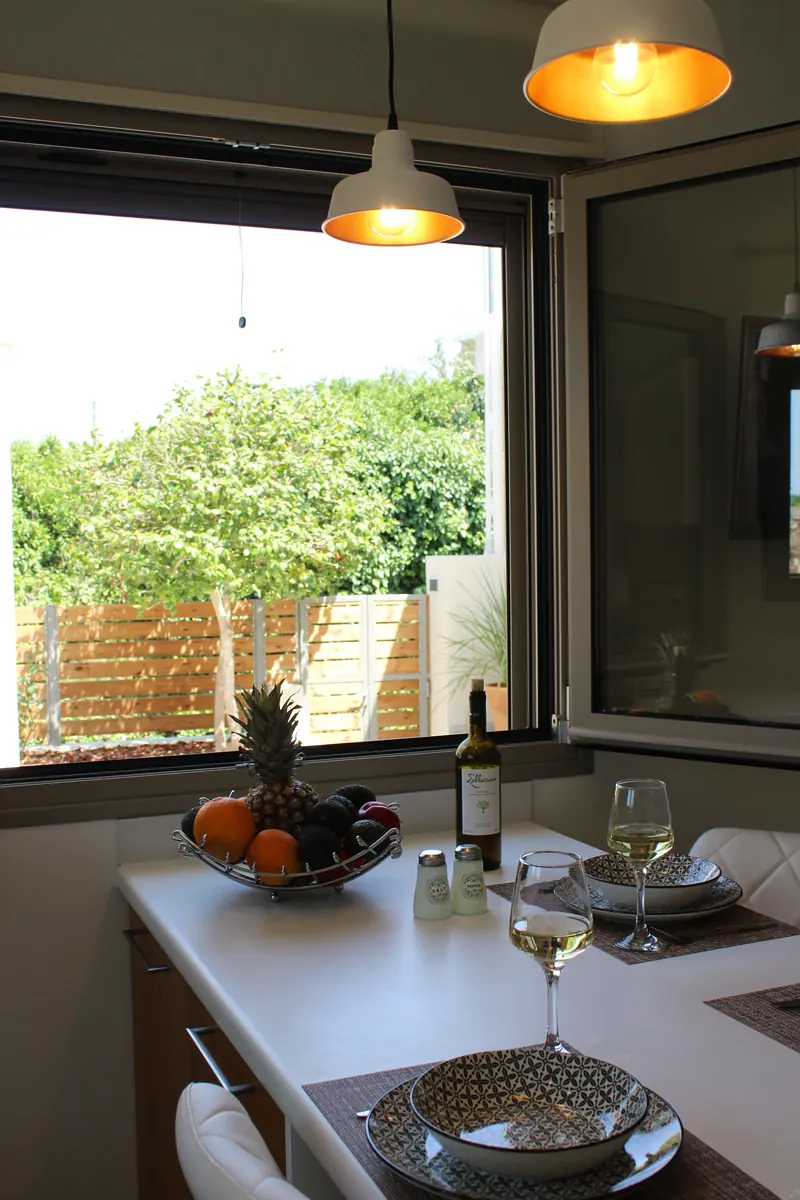 Two pendant lamps lit above the table, a bowl of fruit and a glass of wine by the open window